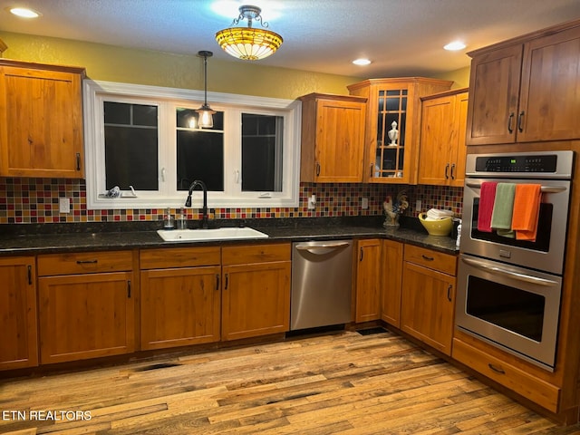 kitchen with light wood-type flooring, tasteful backsplash, stainless steel appliances, sink, and hanging light fixtures