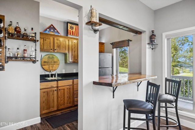 kitchen with dark wood-type flooring, sink, stainless steel refrigerator, and a kitchen breakfast bar