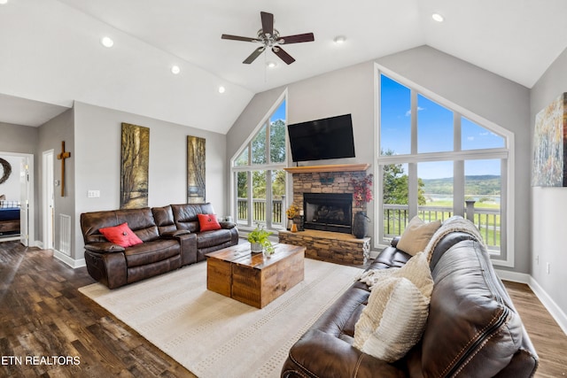 living room with dark hardwood / wood-style flooring, high vaulted ceiling, a stone fireplace, and plenty of natural light