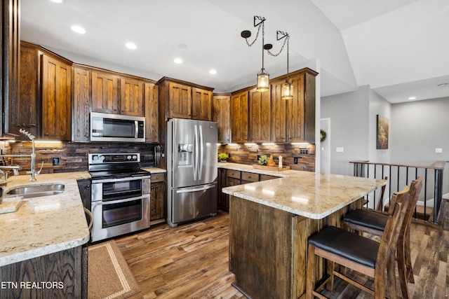 kitchen with tasteful backsplash, appliances with stainless steel finishes, vaulted ceiling, sink, and hardwood / wood-style floors