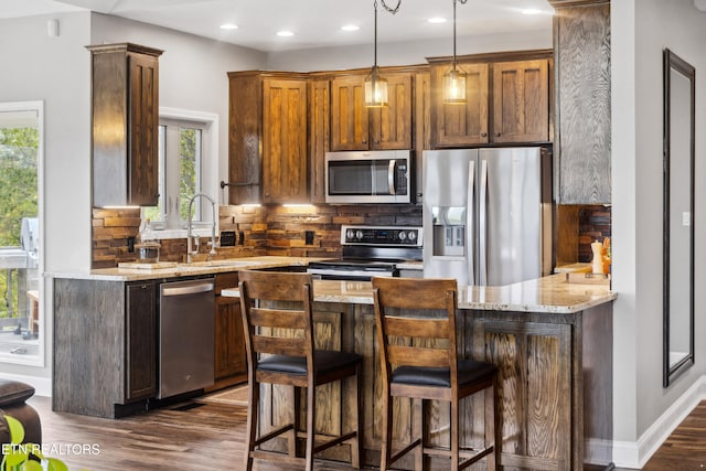 kitchen featuring stainless steel appliances, light stone counters, kitchen peninsula, dark hardwood / wood-style floors, and a breakfast bar