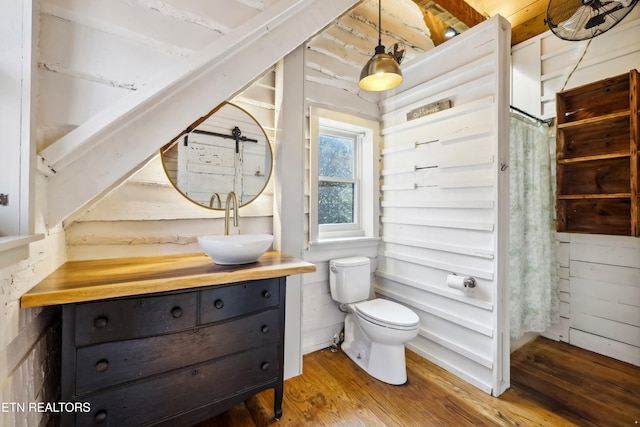 bathroom with hardwood / wood-style floors, wooden walls, toilet, and vanity