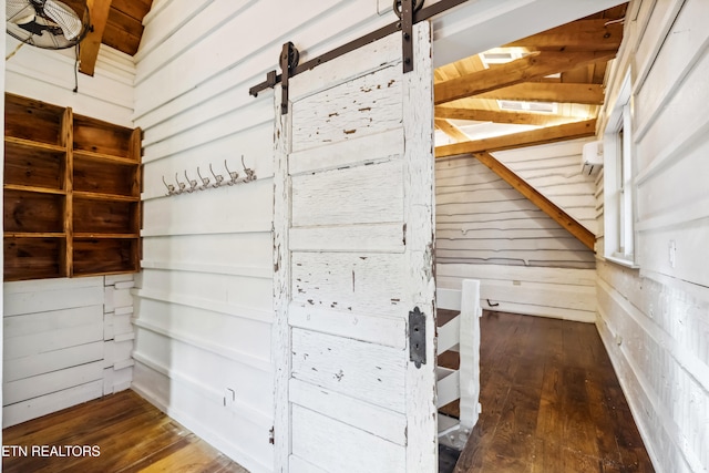 interior space with beam ceiling, wood-type flooring, wooden walls, and a barn door