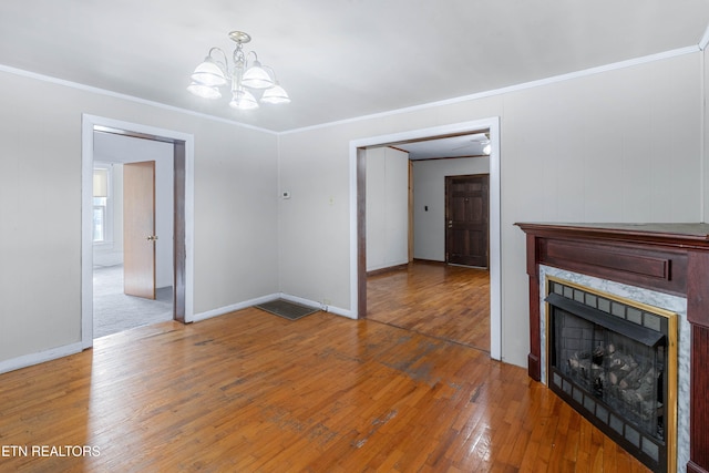 unfurnished living room with an inviting chandelier, a tiled fireplace, hardwood / wood-style floors, and ornamental molding