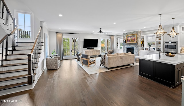 living room with a stone fireplace, ceiling fan with notable chandelier, dark hardwood / wood-style flooring, and ornamental molding