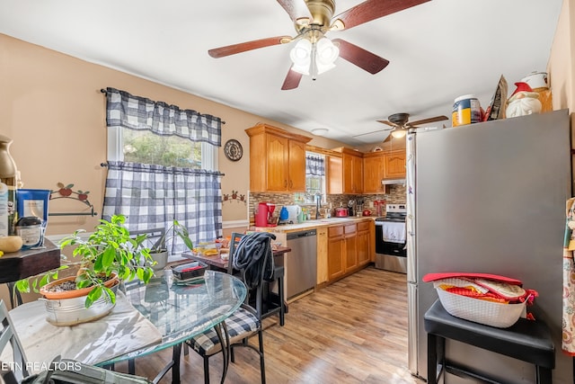 kitchen featuring appliances with stainless steel finishes, decorative backsplash, sink, light hardwood / wood-style floors, and ceiling fan