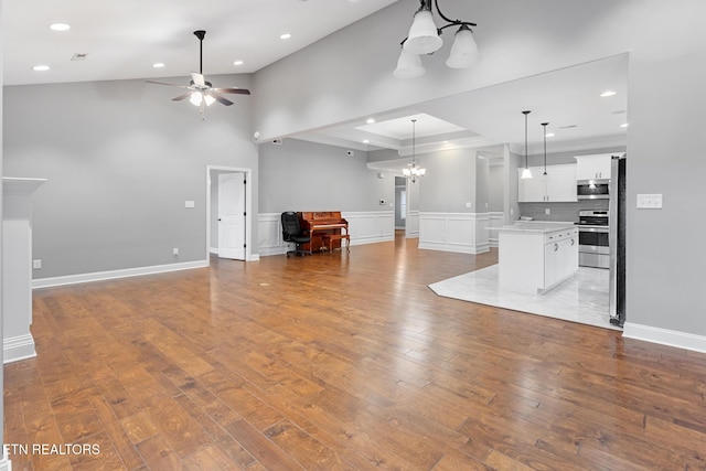unfurnished living room with recessed lighting, ceiling fan with notable chandelier, a high ceiling, hardwood / wood-style flooring, and wainscoting