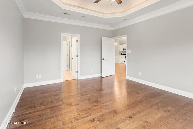 unfurnished bedroom featuring visible vents, crown molding, baseboards, a raised ceiling, and hardwood / wood-style floors