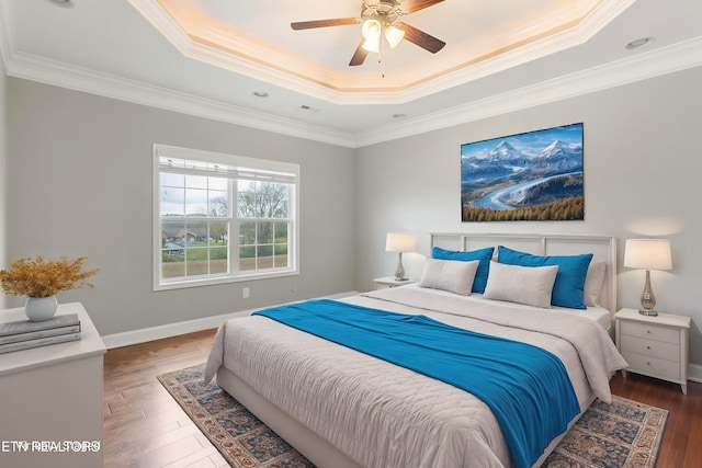 bedroom featuring a tray ceiling, baseboards, crown molding, and wood-type flooring