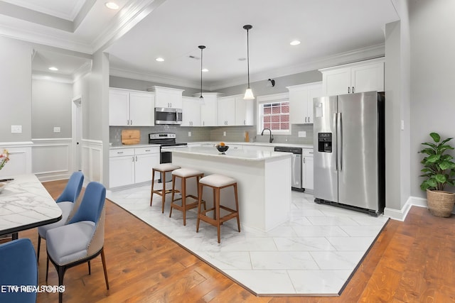 kitchen with appliances with stainless steel finishes, white cabinetry, a kitchen island, and decorative light fixtures