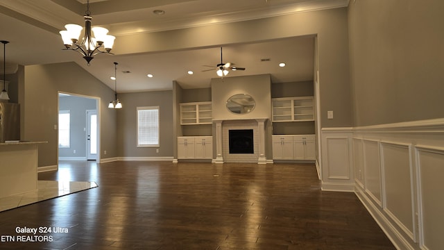 unfurnished living room with lofted ceiling, dark wood-style flooring, ceiling fan with notable chandelier, a fireplace, and wainscoting