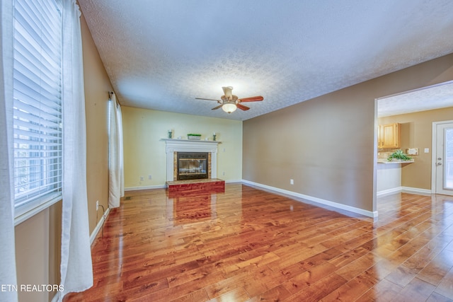 unfurnished living room featuring a brick fireplace, a textured ceiling, hardwood / wood-style flooring, and ceiling fan