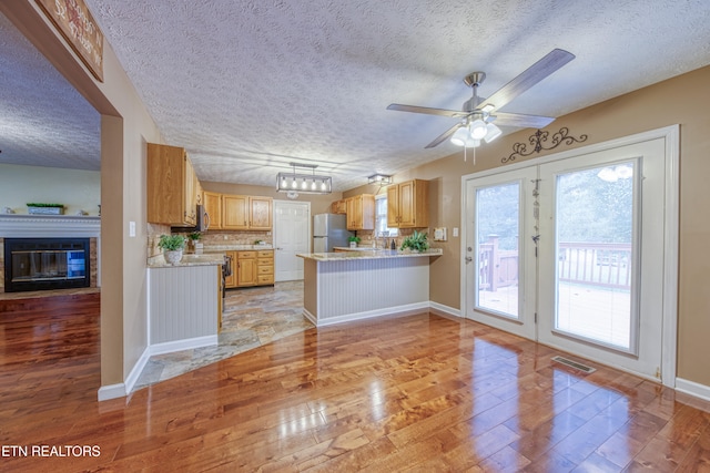 kitchen with a textured ceiling, kitchen peninsula, appliances with stainless steel finishes, and light hardwood / wood-style floors