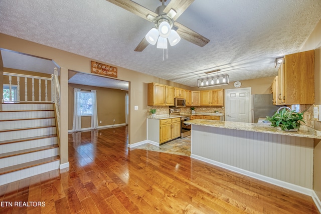 kitchen featuring stainless steel appliances, light hardwood / wood-style floors, kitchen peninsula, a textured ceiling, and decorative backsplash