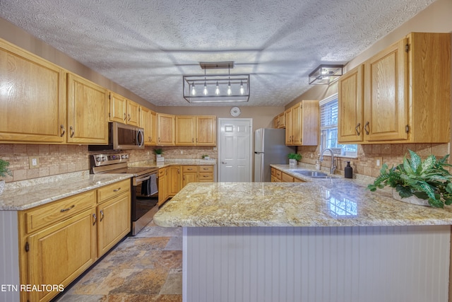 kitchen featuring kitchen peninsula, a textured ceiling, sink, appliances with stainless steel finishes, and decorative light fixtures