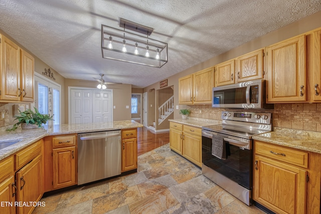 kitchen featuring appliances with stainless steel finishes, tasteful backsplash, light stone countertops, ceiling fan, and a textured ceiling