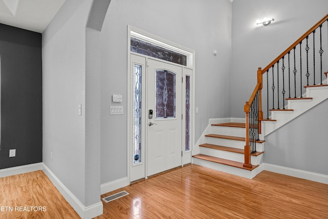 foyer entrance with wood finished floors, visible vents, stairway, arched walkways, and baseboards