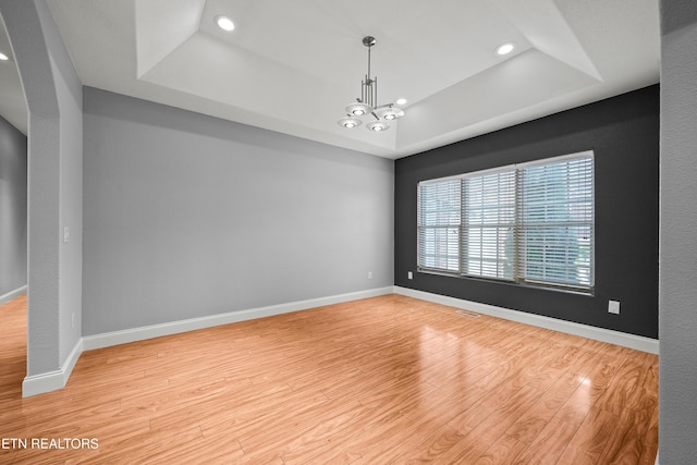 spare room featuring an inviting chandelier, wood finished floors, a tray ceiling, baseboards, and recessed lighting