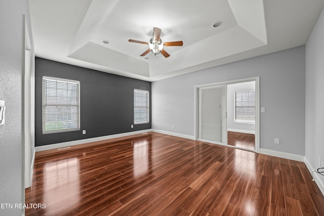 unfurnished room with dark wood-type flooring, ceiling fan, and a tray ceiling