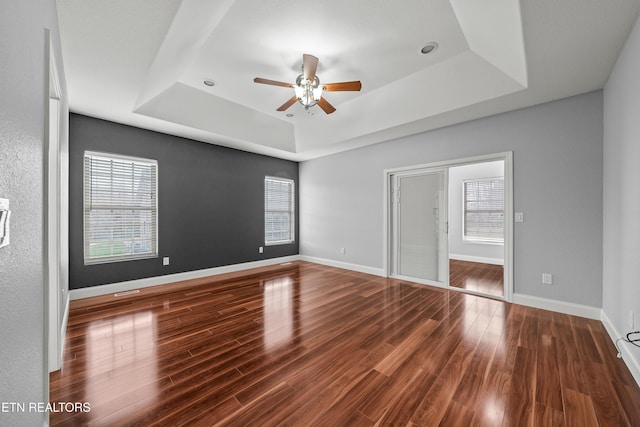 unfurnished bedroom with multiple windows, a tray ceiling, and wood finished floors