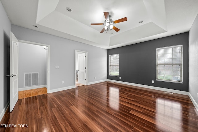 empty room featuring a tray ceiling, ceiling fan, visible vents, and wood finished floors