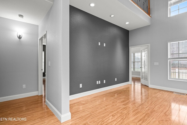 empty room with a high ceiling, baseboards, visible vents, and wood finished floors