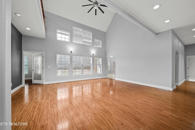 unfurnished living room with a ceiling fan, wood finished floors, high vaulted ceiling, and arched walkways