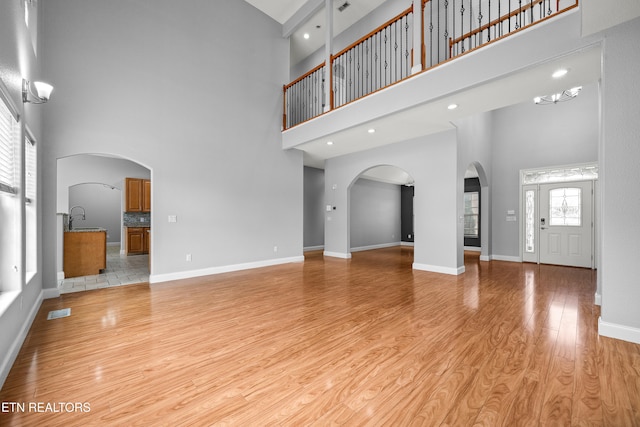 unfurnished living room with light hardwood / wood-style flooring and a towering ceiling