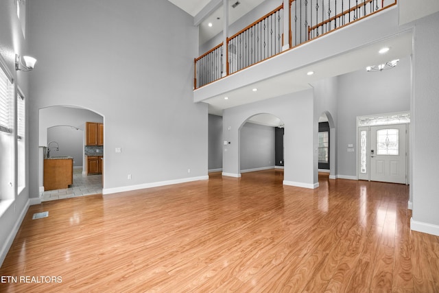 unfurnished living room with a high ceiling, baseboards, light wood-type flooring, and visible vents