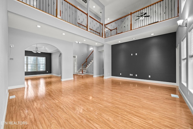 unfurnished living room with a ceiling fan, stairs, wood finished floors, arched walkways, and a high ceiling