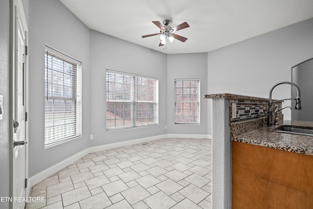 unfurnished dining area featuring wet bar, baseboards, ceiling fan, and a sink
