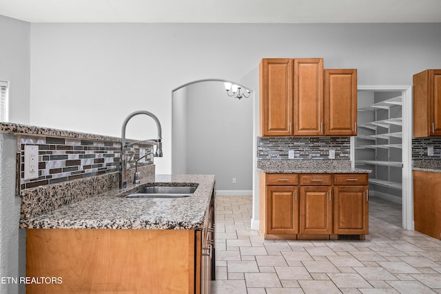 kitchen featuring light stone countertops, baseboards, a sink, backsplash, and brown cabinets