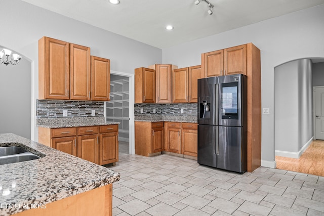 kitchen with a chandelier, tasteful backsplash, light stone counters, and stainless steel fridge with ice dispenser