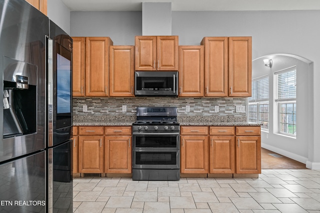 kitchen featuring decorative backsplash, appliances with stainless steel finishes, and dark stone counters