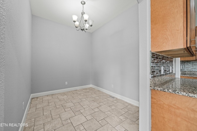 unfurnished dining area with a chandelier and baseboards