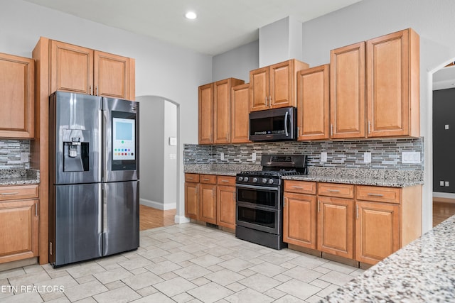 kitchen with baseboards, light stone counters, arched walkways, tasteful backsplash, and appliances with stainless steel finishes