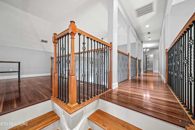 stairway with a chandelier, visible vents, wood finished floors, and baseboards