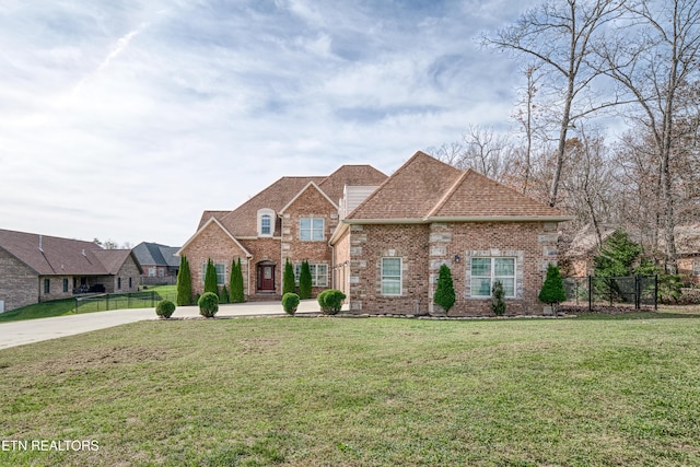 french provincial home featuring a front lawn, brick siding, driveway, and fence