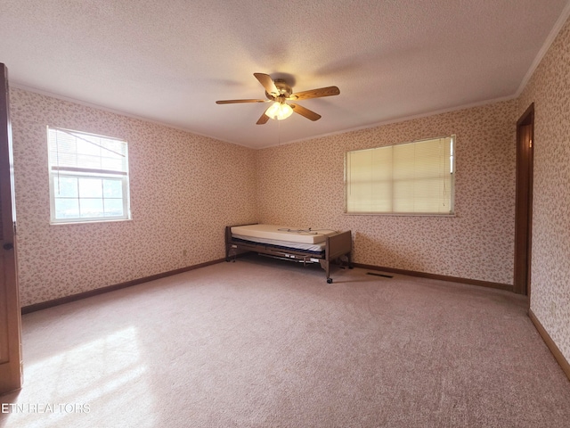 unfurnished bedroom with ceiling fan, a textured ceiling, crown molding, and carpet