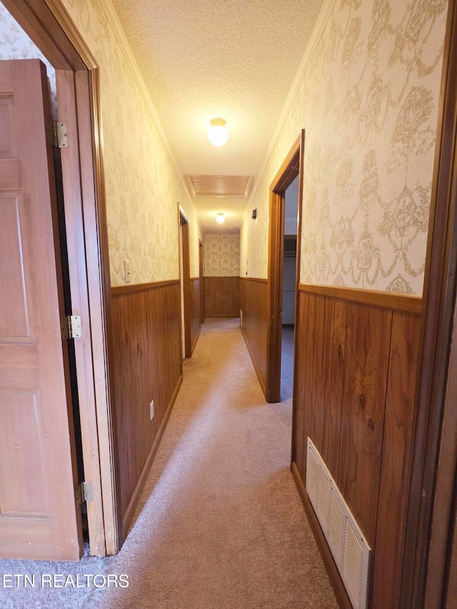 hallway featuring light colored carpet, wood walls, a textured ceiling, and crown molding