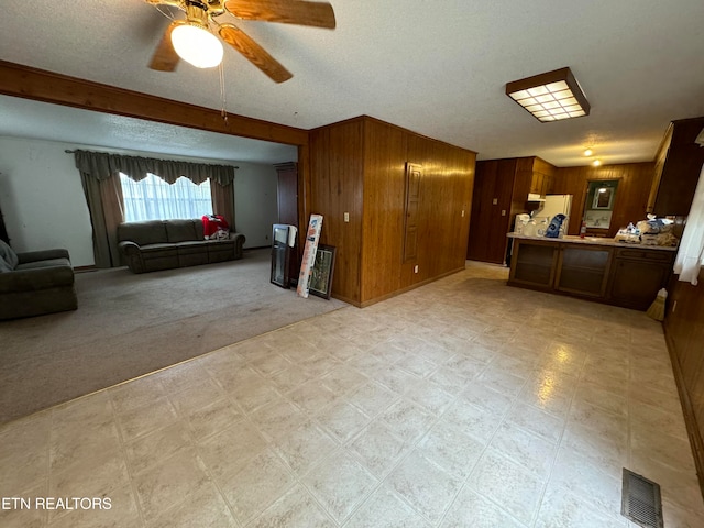 carpeted living room with a textured ceiling, wood walls, and ceiling fan