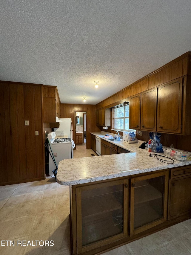 kitchen with a textured ceiling, white appliances, wooden walls, sink, and kitchen peninsula