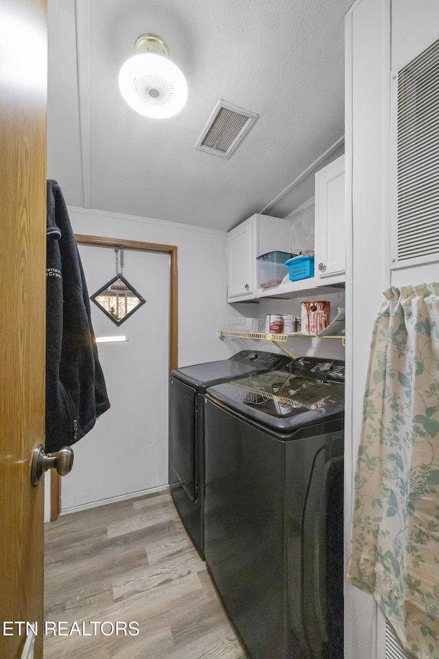 laundry room with a textured ceiling, light wood-type flooring, washer and clothes dryer, and cabinets