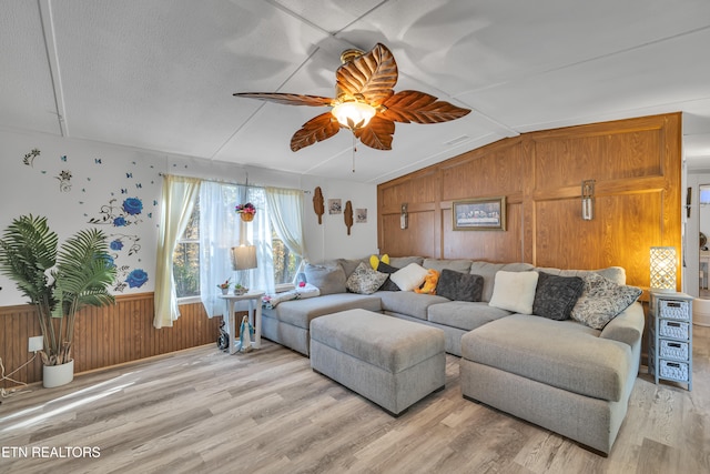 living room featuring wooden walls, vaulted ceiling, ceiling fan, and light hardwood / wood-style flooring