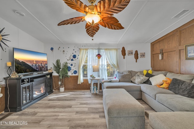 living room with light hardwood / wood-style floors, ceiling fan, and wooden walls