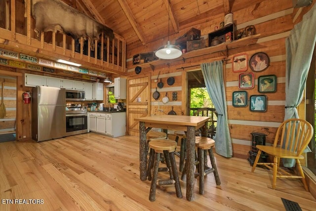 kitchen with stainless steel appliances, white cabinets, wooden walls, light wood-type flooring, and lofted ceiling with beams