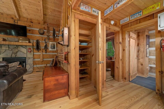 interior space featuring light hardwood / wood-style floors, beam ceiling, a stone fireplace, wood ceiling, and wooden walls