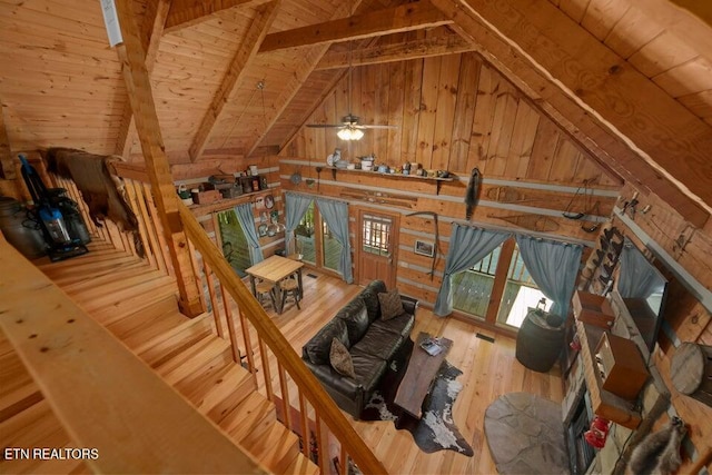 unfurnished living room featuring lofted ceiling with beams, wooden walls, hardwood / wood-style floors, wooden ceiling, and ceiling fan