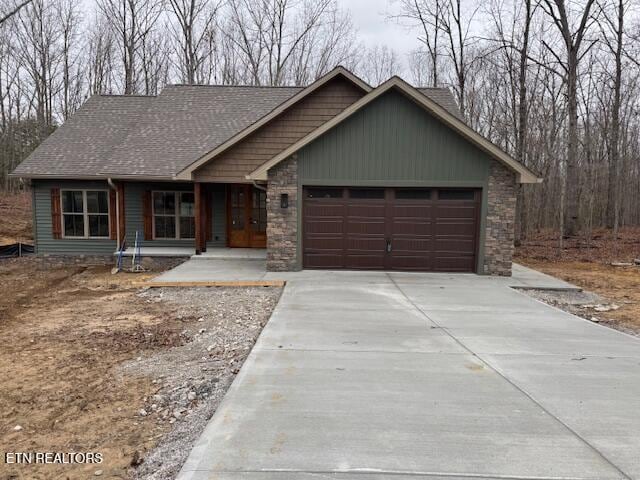 view of front of home with roof with shingles, concrete driveway, covered porch, a garage, and stone siding