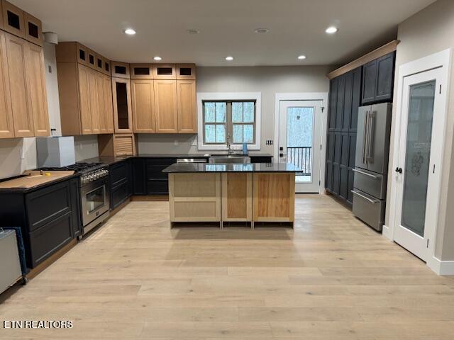 kitchen featuring premium appliances, a sink, light wood-type flooring, a center island, and dark countertops